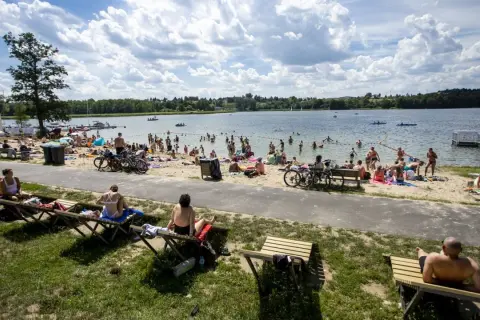 Tłum ludzi odpoczywa nad jeziorem w Poznaniu, opalając się na plaży i kąpiąc w wodzie.
