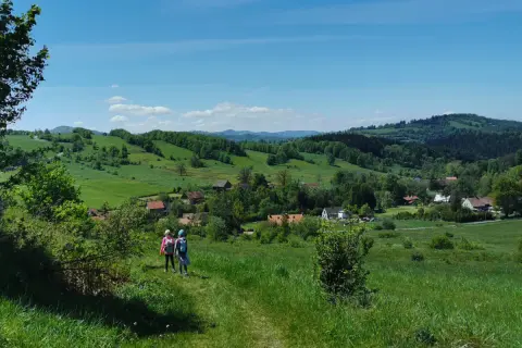 Dwie dziewczynki wędrujące po zielonych wzgórzach Gór Sowich z widokiem na wieś.