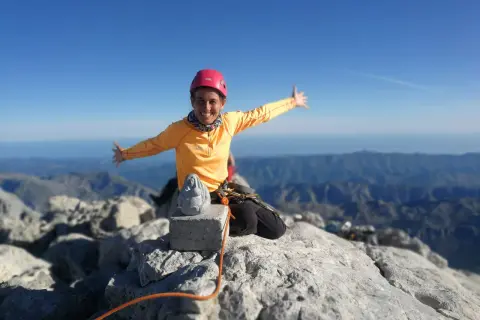Szczęśliwa alpinistka na szczycie góry, z widokiem na pasmo górskie. W tle widać morze. To szczyt Naranjo de Bulnes.