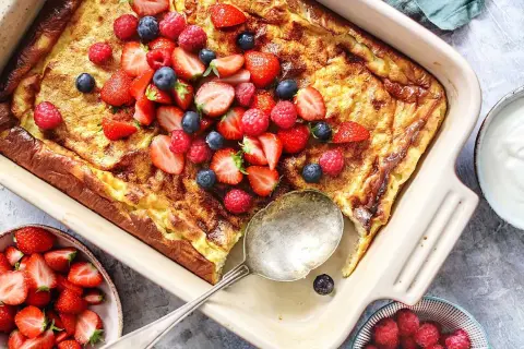 En gyllene ungspankaka toppad med färska jordgubbar, hallon och blåbär. Serveras med en skål bär och gräddfil.
