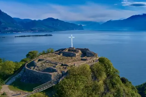Rovine di un castello con una croce bianca su una collina a Manerba del Garda. Vista panoramica sul Lago di Garda e le montagne.