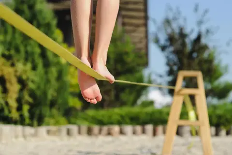 Füße balancieren auf einer gelben Slackline, die an einem Holzgestell befestigt ist.
