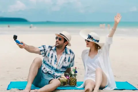 Para na plaży robi selfie z kamerką GoPro, ciesząc się wakacjami. W tle błękitne morze i niebo.