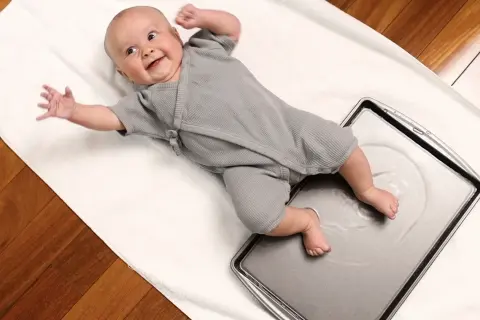 Joyful baby giggles during water play, kicking tiny feet in a shallow pan.