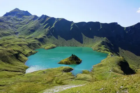 Türkiser Bergsee in Deutschland mit einer kleinen Insel, umgeben von grünen, schattigen Berghängen.