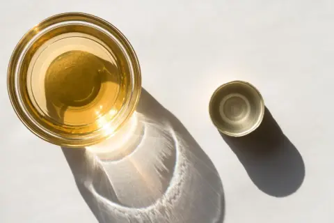 Ein Glas mit goldenem Apfelessig steht neben seinem Deckel. Sonnenschein wirft interessante Schatten. Bereit, Apfelessig zu trinken.