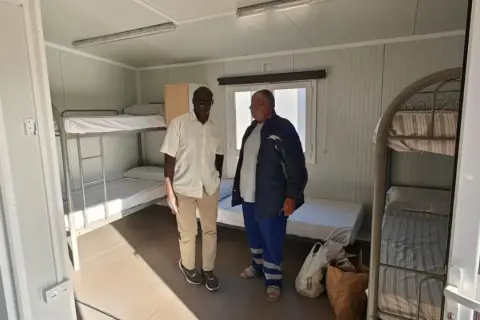 Dos hombres observan literas en un alojamiento temporal, un ejemplo de trabajo a cambio de alojamiento.