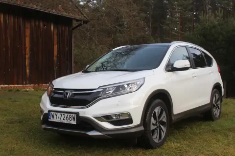 Biały Honda CR-V 2.0 benzyna zaparkowany na trawie obok drewnianej stodoły.
