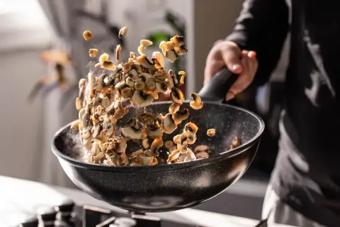 Man salteando champiñones en una sartén, mostrando cómo cocinar las setas para un plato delicioso.