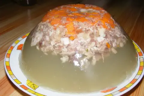 Tradycyjna galareta wieprzowa z kawałkami mięsa i marchewki, w galaretce, na talerzu.