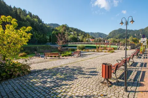 Promenada nad Grajcarkiem zachęca do spaceru. Ławki, latarnie i brukowana ścieżka w otoczeniu zieleni i gór.