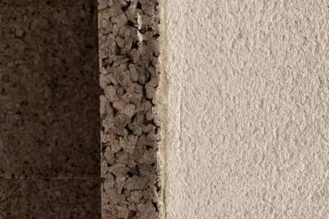Dettaglio di un muro con strato di intonaco con sughero grezzo e finitura chiara e ruvida.