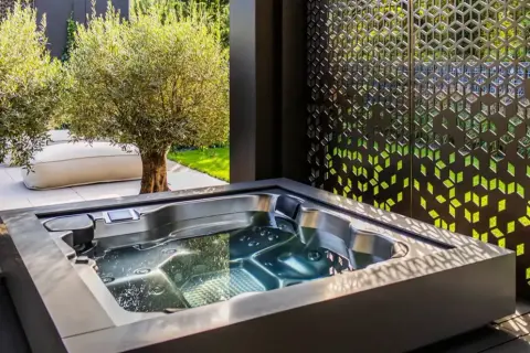 Un jacuzzi moderno en un jardín con olivos y un biombo decorativo. El lugar perfecto para un momento de relax y qué es un chill out.