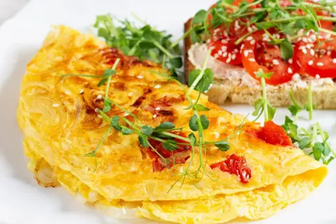 Złocisty omlet z pomidorami, posypany sezamem, podany z tostami i kiełkami. Pyszne śniadanie.