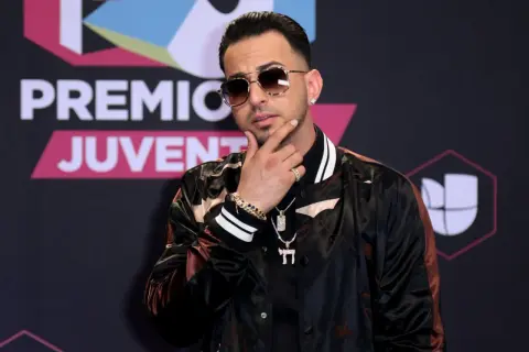 Justin Quiles poses with his hand on his chin, wearing sunglasses and a stylish jacket at Premios Juventud.