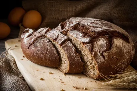 Pane di segale affettato su tagliere, con uova e spighe. Attenzione, il pane di segale fa ingrassare se consumato in eccesso.