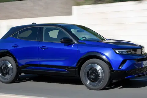 Błękitny Opel Mokka 2024 z czarnym dachem pędzi po drodze, prezentując swój nowoczesny design i dynamiczną sylwetkę.