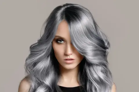 Frau mit voluminösem, welligem Haar in einem modernen balayage grau Farbton.
