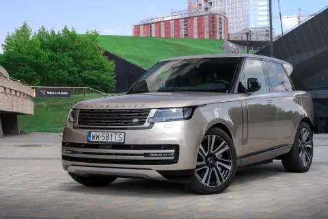 Elegancki Range Rover 2025 w kolorze piaskowym prezentuje się na tle nowoczesnej architektury.