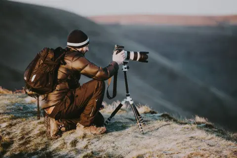 Un homme, peut-être le plus grand photographe du monde, s'accroupit sur une colline gelée, ajustant son appareil photo professionnel sur un trépied pour capturer le paysage.