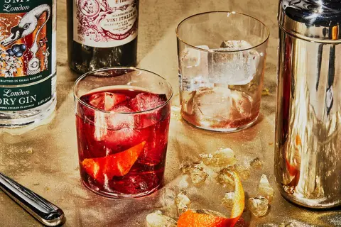 Zutaten für einen Negroni: Gin, roter Wermut und Campari. Serviert mit Eis und Orangenzeste.