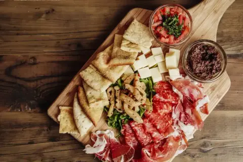 Un beau plateau de charcuterie avec jambon, salami, fromages, pain, olives et tomates.
