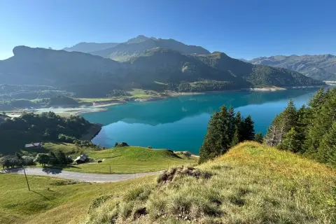 Vue panoramique du lac de la Gittaz aux eaux turquoise, entouré de montagnes verdoyantes et d'une route sinueuse.