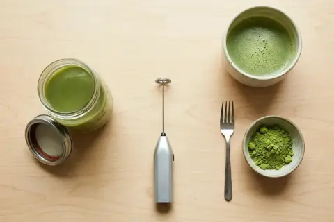Préparation du matcha sans fouet : poudre verte, boisson mousseuse dans un bol, et un petit appareil argenté pour mélanger.