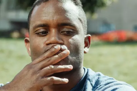 Uomo con mano sulla bocca, pensieroso. Il gesto di coprirsi la bocca può avere un **sputare significato psicologico** di repressione o riflessione interiore.