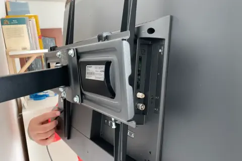 Montaż uchwytu do telewizora na ścianie z regipsu. Widoczne śruby i złącza.
