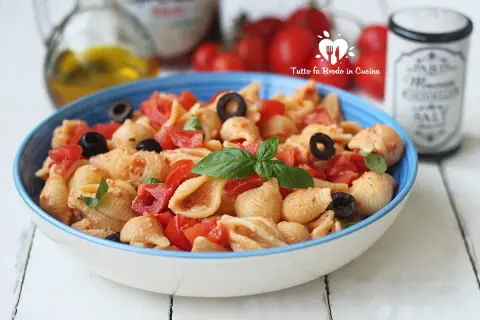 Un piatto di pasta con ricotta e pomodorini freschi, arricchito da olive nere e basilico.