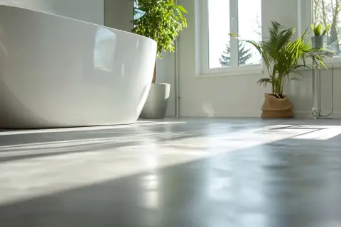 Solen lyser upp ett modernt badrum med fristående badkar och växter. Golvet är av microcement på våtrumsmatta, vilket ger en stilren och hållbar yta.