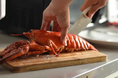 Préparation d'un homard pour un accompagnement homard froid. Une main tient le homard pendant qu'une autre le coupe sur une planche à découper.