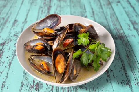 Un plat de moules au roquefort, garni de persil frais, baignant dans une sauce crémeuse. Un délice à savourer.