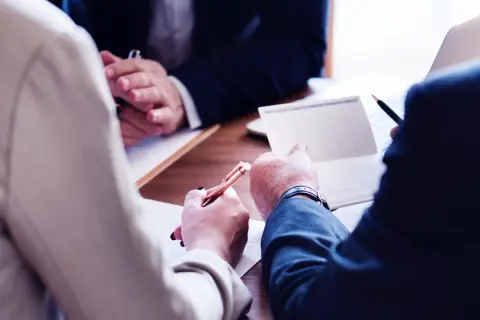 Mötesdeltagare diskuterar dokument och antecknar, kanske för att hantera en force majeure i Sverige.
