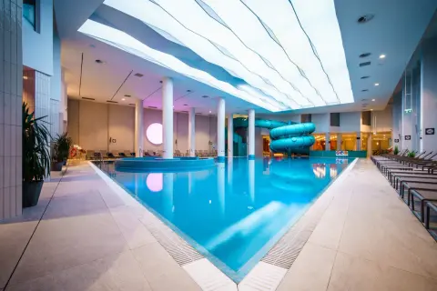Basen z atrakcjami wodnymi w hotelu Gołębiewski Wisła. Błękitna woda, zjeżdżalnie i nowoczesny sufit.