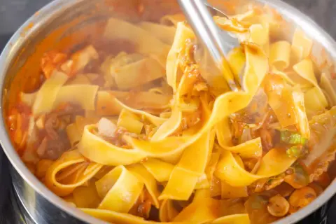Szybki obiad z makaronem w sosie pomidorowym z warzywami. Gorące, parujące tagliatelle w garnku, gotowe do podania.