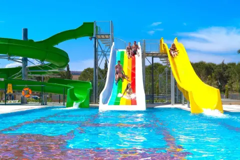 Wesoła zabawa na zjeżdżalniach wodnych w Venosa Beach Resort & Spa. Dzieci i dorośli ścigają się po tęczowej i żółtej zjeżdżalni, wpadając do basenu.