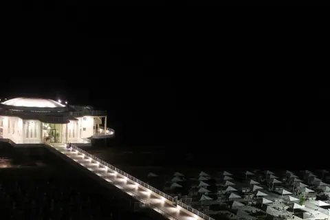 La Rotonda a Mare di Senigallia illuminata di notte, con la passerella che conduce all'edificio e la spiaggia con ombrelloni chiusi.