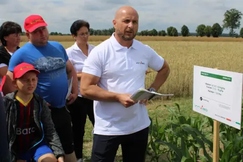 Grupa ludzi na polu kukurydzy, gdzie prezentowane są środki ochrony roślin, w tym metkonazol.