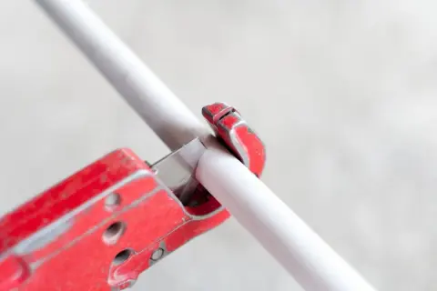 A red pipe cutter is shown in action, demonstrating how to cut PVC pipe cleanly and efficiently.
