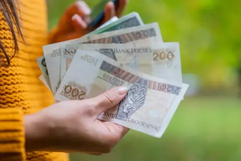 Dłoń trzyma polskie banknoty 200 zł. Zastanawiasz się, ile to netto po przekroczeniu drugiego progu podatkowego?