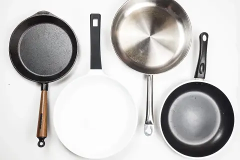 Vier Pfannen: Gusseisen, weiß beschichtet, Edelstahl und eine weitere beschichtete Pfanne. Jede aluminium oder edelstahl pfanne hat ihren Zweck.