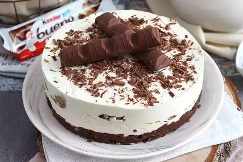 Pyszna tarta Kinder Bueno z kremem i czekoladowymi wiórkami, ozdobiona batonikami.