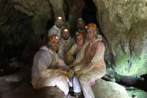 Grupo de exploradores sonríe dentro de la Cova do Rei Centolo, equipados con cascos y trajes protectores.