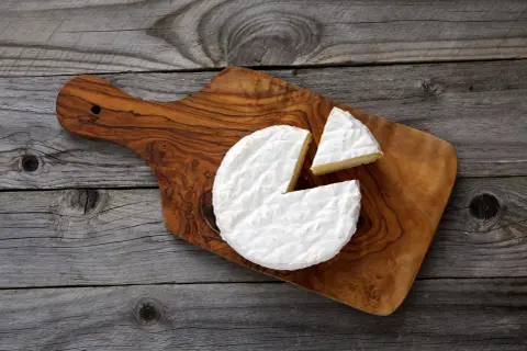 Un morceau de **brie** crémeux, avec une part coupée, sur une planche en bois rustique.