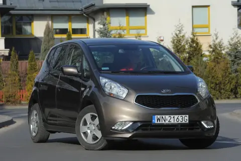 Brązowa Kia Venga z nowymi żarówkami LED, zaparkowana przed nowoczesnym domem.