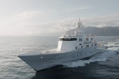 L'alessandro del bono yacht solca le onde con eleganza, un gioiello bianco su un mare calmo, con montagne sullo sfondo.