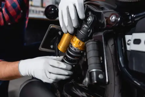 Mains gantées ajustant un amortisseur doré sur une moto. Faut-il changer les 4 amortisseurs pour une meilleure tenue de route ?