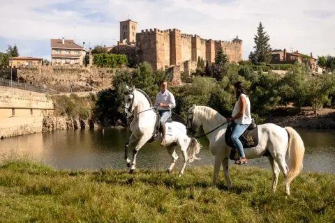 Paseo a caballo junto al río en Buitrago de Lozoya, con el castillo medieval al fondo.